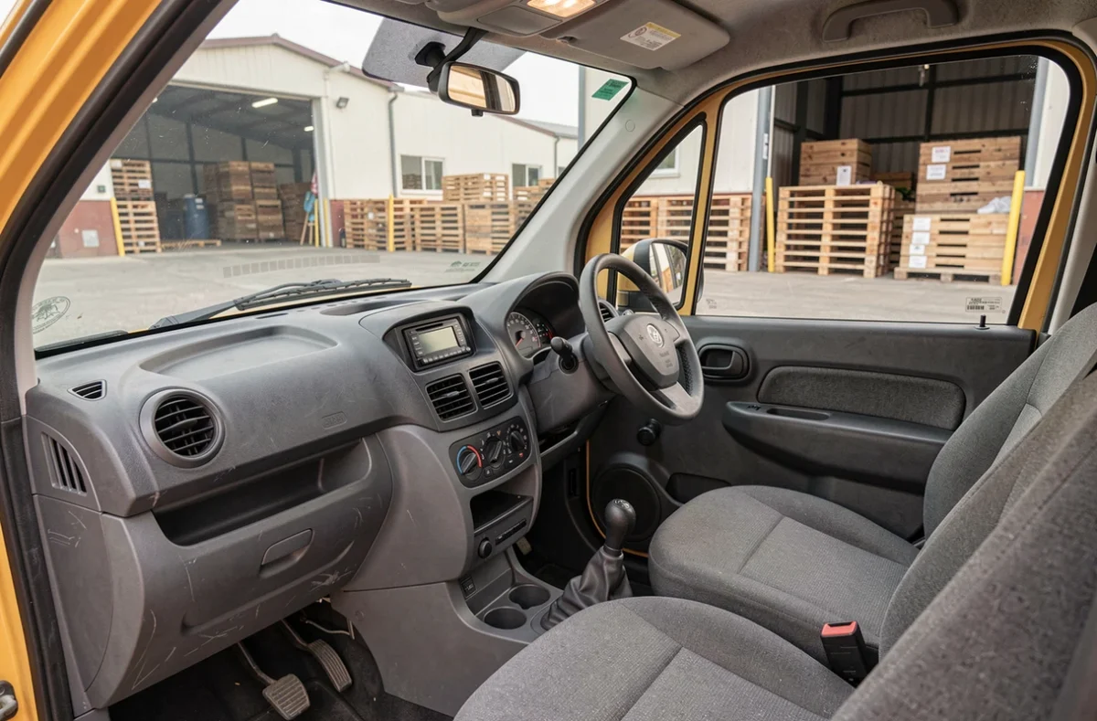 Intérieur de l'habitacle d'une voiture sans permis utilitaire avec tableau de bord simple et vue sur un quai de chargement