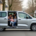 Grande famille réunie autour d'un Peugeot Partner Tepee gris garé dans une rue résidentielle, parents et enfants découvrant l'habitacle spacieux