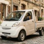 Voiture sans permis utilitaire blanche chargée de colis de livraison, garée dans une rue pavée commerçante